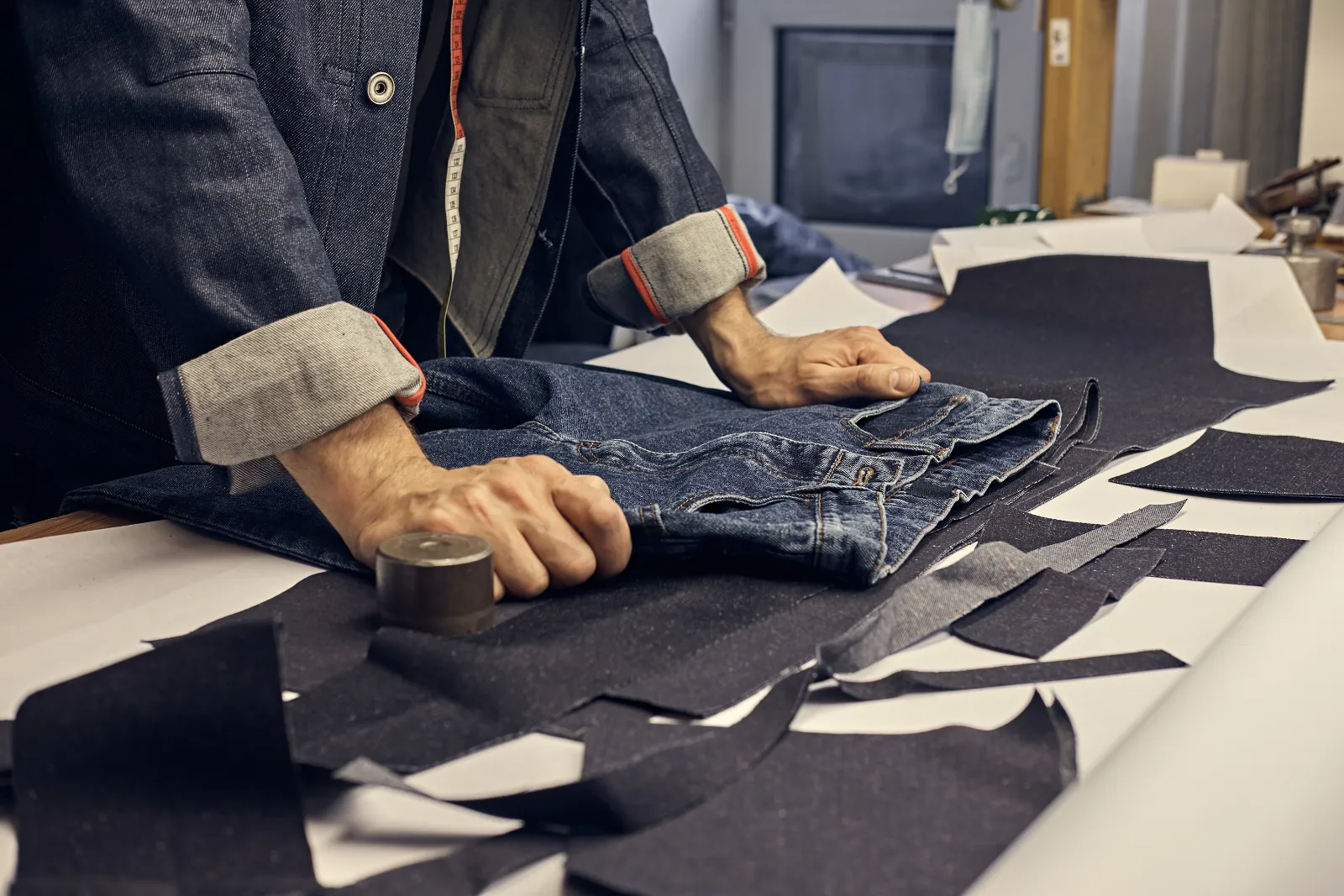 Schneider misst eine Jeans mit dem Maßband ab, um die Hose zu kürzen
