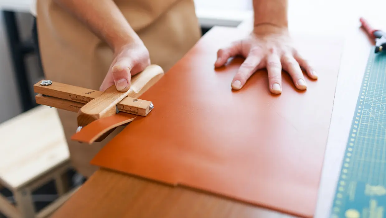 Hände beim Zuschneiden von braunem Leder auf dem Arbeitstisch
